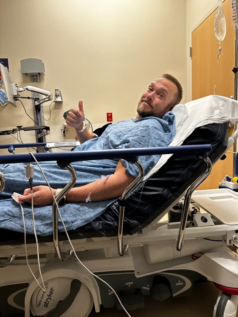 Nick giving a thumbs-up from a hospital bed at his lowest point