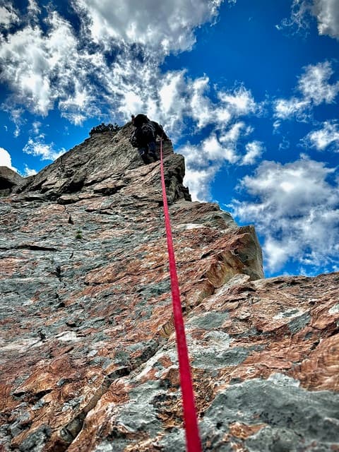 A climber high on a rock ridge, with the rope dropping toward the camera